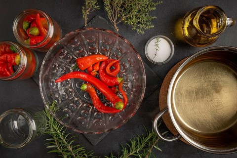 Hot peppers in jars and bowl, next to it an open cooking pot on a dark background