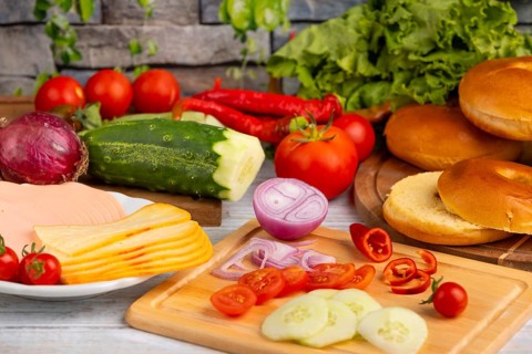 Bagels alongside sausage, cheese and fresh vegetables such as tomatoes, lettuce, cucumber and