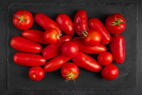 Different types of tomatoes lie on a dark slate slab