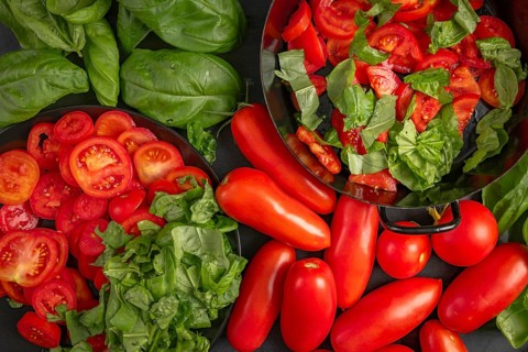 Pan and plate with sliced tomatoes and basil leaves, surrounded by fresh vegetables