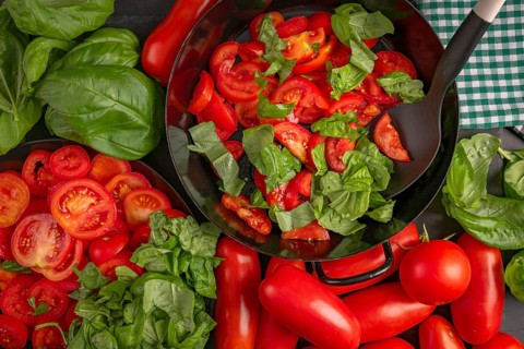 A pan filled with sliced tomatoes and basil leaves, surrounded by fresh vegetables