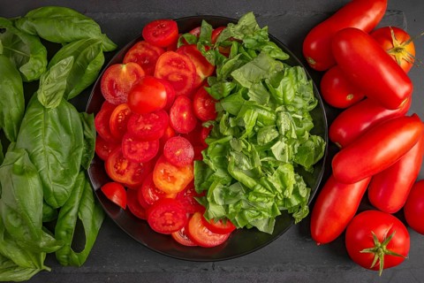 Sliced tomatoes and basil on a black plate