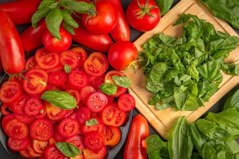 Fresh tomatoes and basil leaves on a chopping board, in bright red and green colours