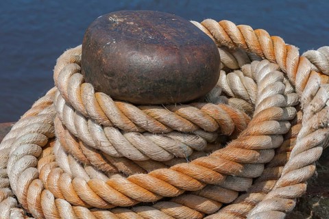 Ropes knotted around a metal bollard, beige and brown, rich in contrast against a dark blue