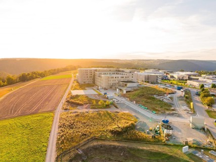 Building situated in gently rolling landscape with fields, illuminated by sunset, new hospital