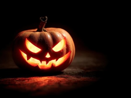 A spooky carved glowing pumpkin in a dark room, symbolising Halloween and autumnal mood, AI