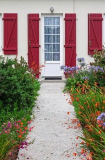 House façade with mullioned windows, entrance door and red shutters and flower beds, Ile de Brehat,