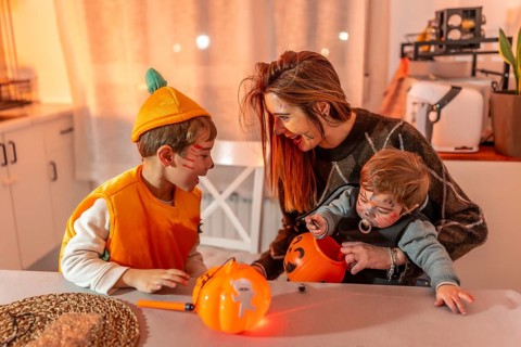 Mother and children wearing halloween costumes are sitting at a table in their kitchen, playing