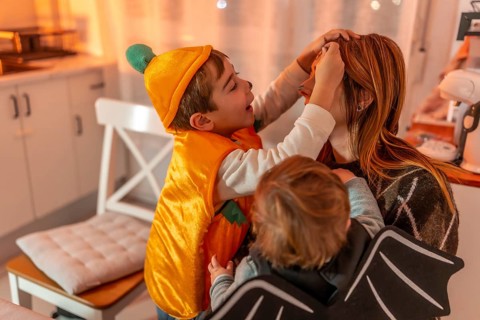 Two brothers, dressed up in halloween costumes, applying makeup on their mother's face, creating a