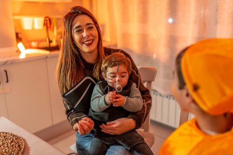 Mother holding her baby dressed up as a bat while smiling at her other child dressed in orange