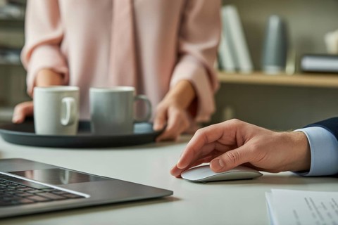 Woman holding a tray with white coffee mugs next to a man's hand on a large wireless mouse. Gender