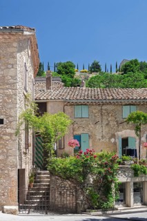 A rustic house with a terrace decorated with flowers, shutters and green hills in the background,