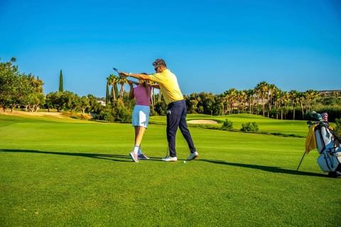 Middle aged golf instructor assisting young woman golfer on improving her swing on a sunny day at