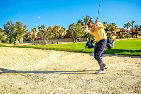Professional golfer hitting a ball out of a sand trap on a sunny day, showcasing skill and