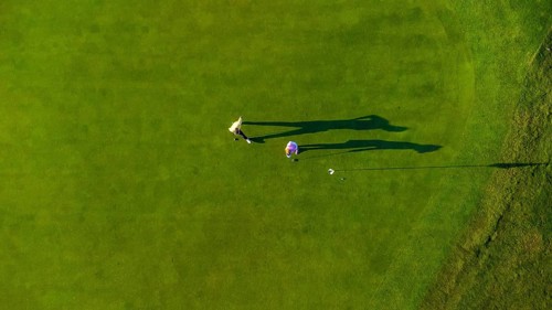 Two golfers are putting on a vibrant green golf course, seen from an aerial perspective, creating