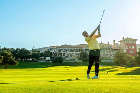 Professional golfer swinging his club, hitting a golf ball on a lush green course, with a luxury