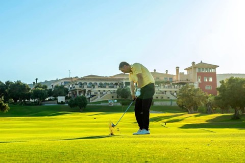 Golfer takes a swing, sending the ball flying across a vibrant green golf course, with a luxurious