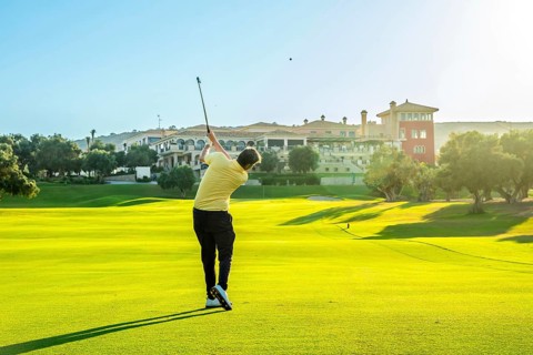 Golfer hitting a shot on a beautiful, sunny golf course with a luxury resort in the background