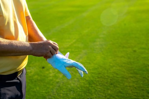 Golfer putting on a white glove, getting ready for an exciting game on a lush, vibrant green golf