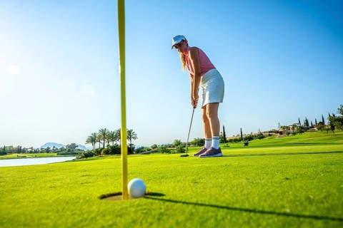 Woman focusing on a putt on a bright, sunny day at a lush golf course, with a ball near the hole