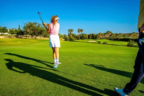 Woman golfer swinging her club on a sunny golf course, preparing to hit the ball towards the hole