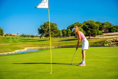 Female golfer concentrating on putting the ball on a sunlit day, enjoying the beauty of a lush golf