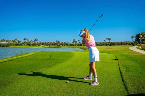 Woman golfer focusing intently on putting the ball on a sunny day, with a picturesque lake creating