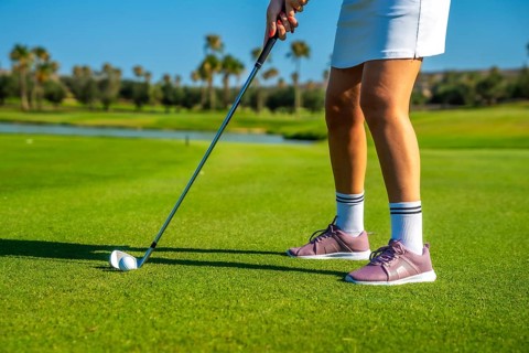 Female golfer concentrating intensely while hitting the golf ball on a bright, sunny day at the