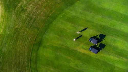Aerial view of two golfers playing on a perfectly manicured green golf course, enjoying a sunny day
