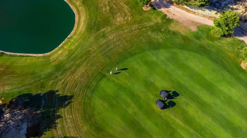 Scenic aerial view of a golf course featuring two players walking near golf carts on a lush green