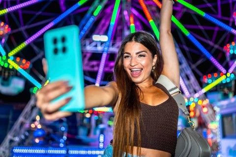 Young woman taking a selfie with smartphone in front of a colorful ferris wheel at an amusement