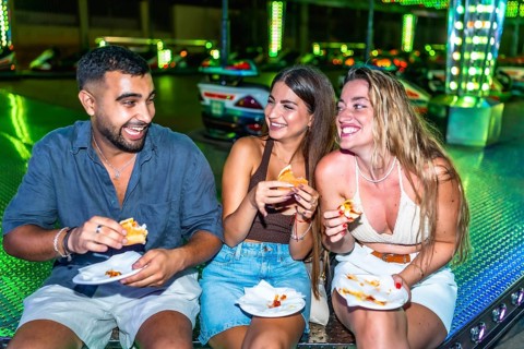 Happy friends enjoying burgers and pizza at amusement park, having fun together on a summer night
