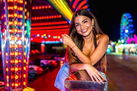 Happy young woman enjoying the vibrant atmosphere of a funfair, posing near colorful attractions at