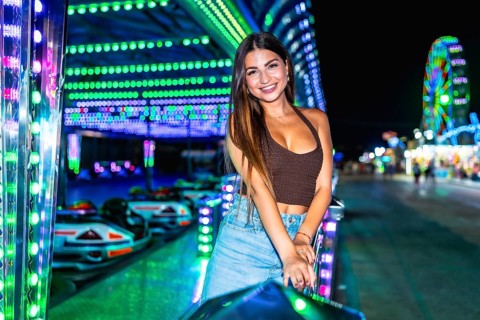 Happy young woman posing joyfully near vibrant, illuminated bumper cars at an amusement park,