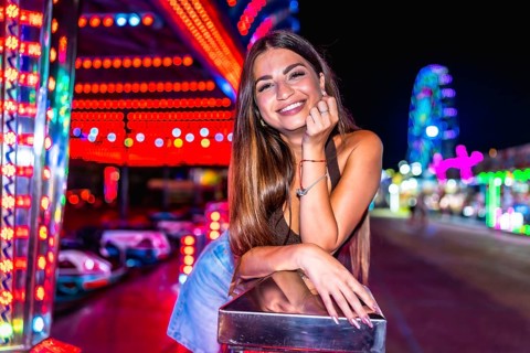 Happy woman enjoying night at amusement park, leaning on railing with colorful bumper cars and