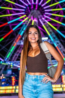 Happy young woman posing at night with illuminated ferris wheel in background, enjoying funfair