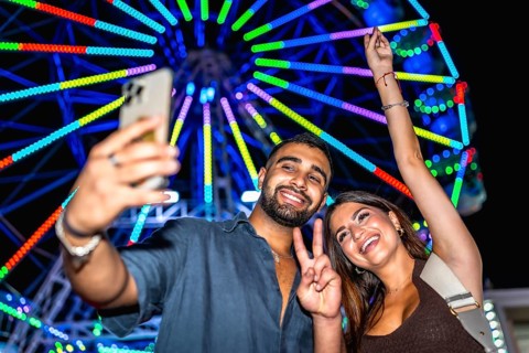 Joyful friends capturing a selfie with a vibrant ferris wheel in the background, celebrating a fun