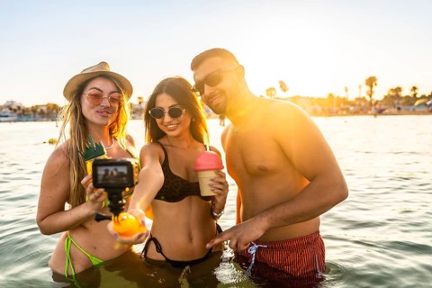 Three friends enjoying summer vacation, taking a selfie with action camera in the sea at sunset,