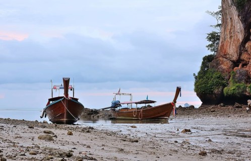 Two traditional thai longtail boats sit peacefully on the shore of railay beach, krabi, thailand,