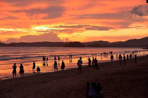 Tourists strolling along a picturesque beach in thailand at sunset, soaking in the vibrant orange