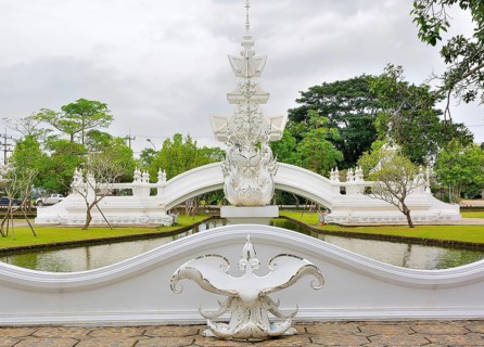 Ornate white bridge reflecting beautifully in the tranquil canal of a thai temple, surrounded by