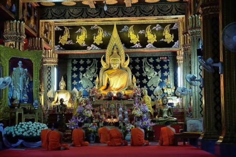 Group of buddhist monks praying in traditional orange robes inside ornate temple with golden buddha