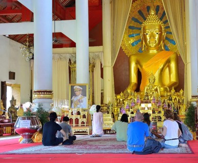 Tourists kneeling and praying in front of a giant golden buddha statue inside a buddhist temple in