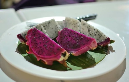 Vibrant slices of red and white dragon fruit are presented on a banana leaf atop a white plate,