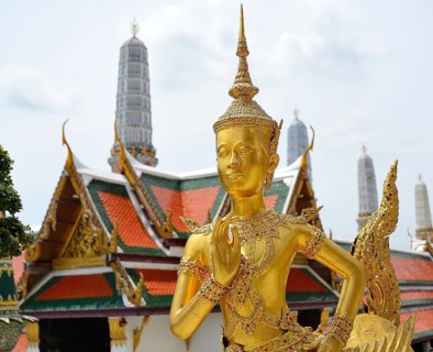 Golden kinnara statue praying with hands joined in a traditional thai greeting, inside the wat phra