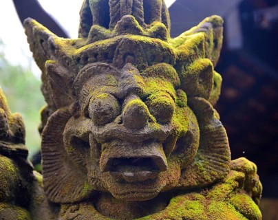 Close up of a weathered traditional balinese stone statue covered in moss, showcasing the rich