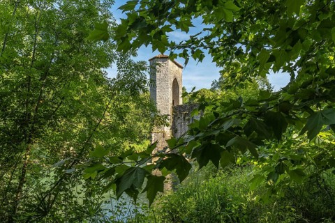 Green leaves frame a medieval bridge tower in sauveterre de bearn, france, creating a picturesque