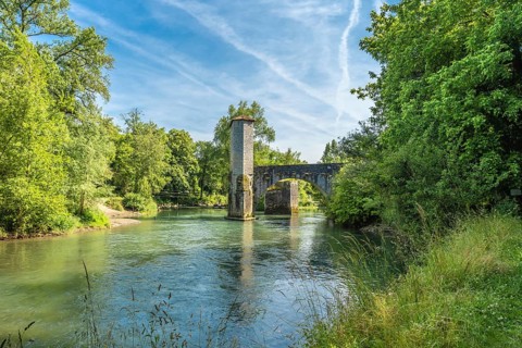 Scenic view of the historic stone bridge over the gave d'oloron river, surrounded by lush greenery,