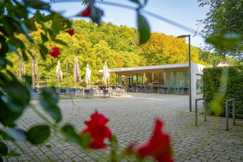 Café with open terrace, framed by lush greenery and red flowers in the foreground, Nagold, district