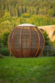 Large wooden ball in a park, surrounded by green grass and trees in the background, Nagold,